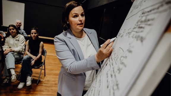 Dozentin beschriftet Whiteboard vor Studierenden
