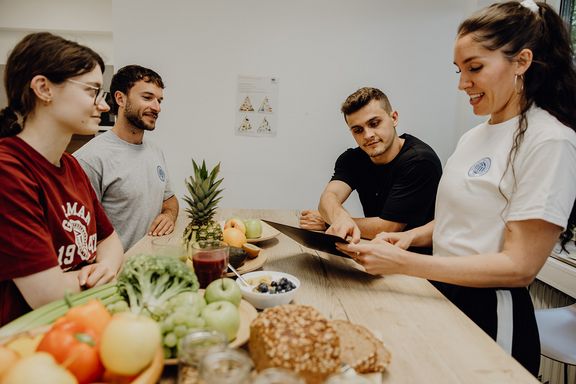 Gruppe von Menschen steht um einen Tisch mit gesunden Essen
