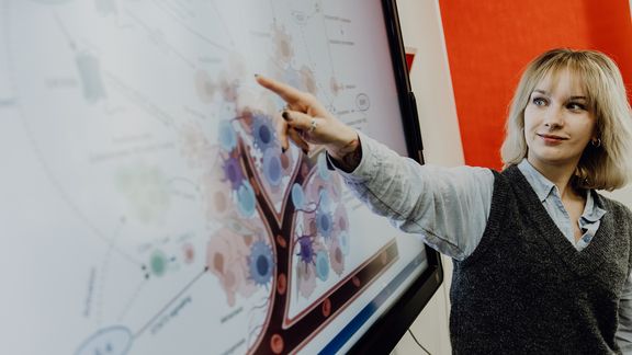 Person deutet auf Grafik in einer Präsentation am Monitor
