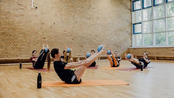 Trainerin und Gruppe machen Pilates Übung in einer Turnhalle
