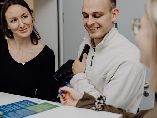 Foto von drei Personen die einen Flyer auf dem Tisch betrachten
