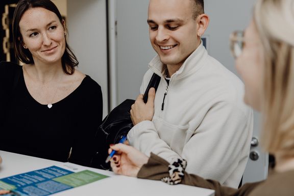 Foto von drei Personen die einen Flyer auf dem Tisch betrachten

