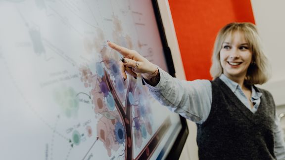 Person deutet auf Grafik in einer Präsentation am Monitor
