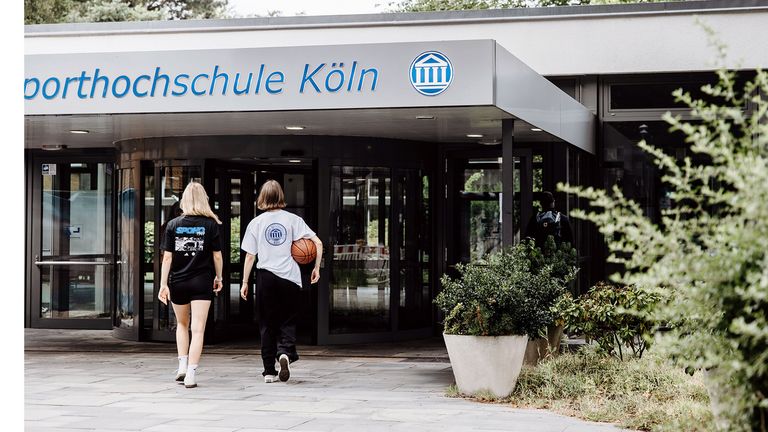 Zwei Studentinnen betreten die Uni über den Haupteingang
