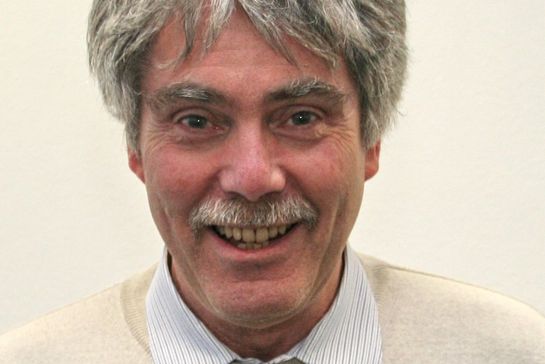 ältere Person mit grauen Haaren und Schnauzbart lächelt in die Kamera