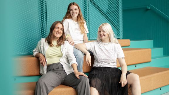 Drei Frauen sitzen auf einer Bank und schauen in die Kamera
