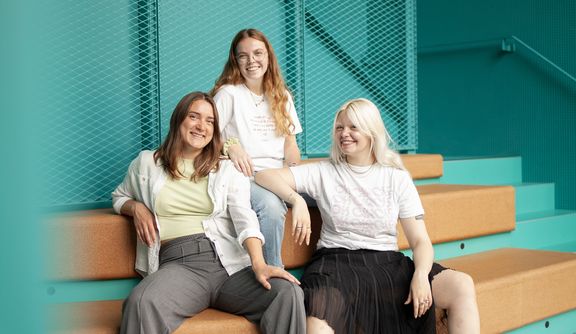 Drei Frauen sitzen auf einer Bank und schauen in die Kamera

