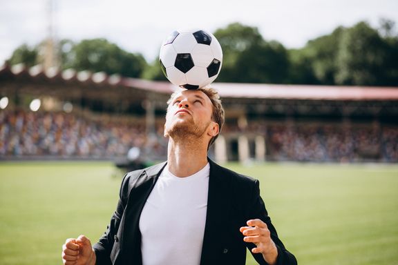 Manager balanciert Fußball auf dem Kopf.
