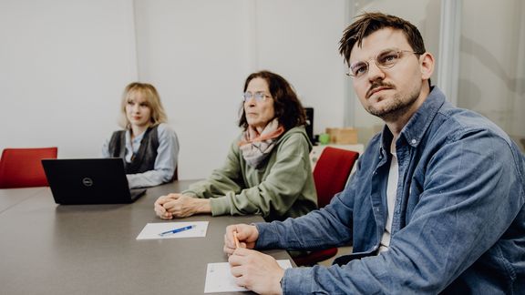 Personen blicken im Konferenzraum sitzend nach vorne

