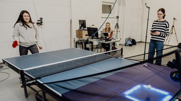 Probandin führt Tischtennisaufschlag auf einer Platte in Richtung eines leuchtenden Quadrats auf der anderen Seite aus
