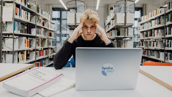 Student blickt verzweifelt auf seinen Laptop in der Bibliothek
