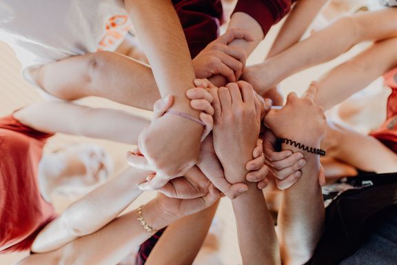 Mehrere Kinder legen ihre Hände übereinander und bilden gemeinsam einen Kreis. Die Nahaufnahme vermittelt Teamgeist, Zusammenarbeit und Gemeinschaft.
