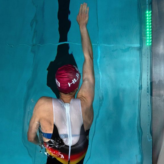 Schwimmer von oben gesehen, Arm nach vorne gestreckt, im Wasser einer Schwimmbahn mit schwarzer Bahnmarkierung. Am Beckenrand leuchtet eine grüne Lichtlaufleiste zur Zeitmarkierung
