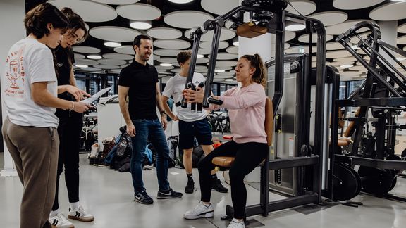 Studierende beobachten Studentin beim Krafttraining 
