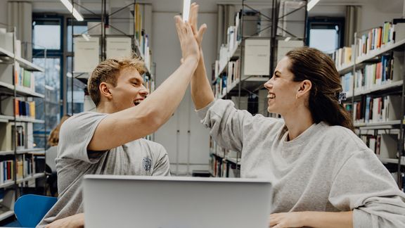 Zwei Studierende geben sich ein High-Five in der Bibliothek
