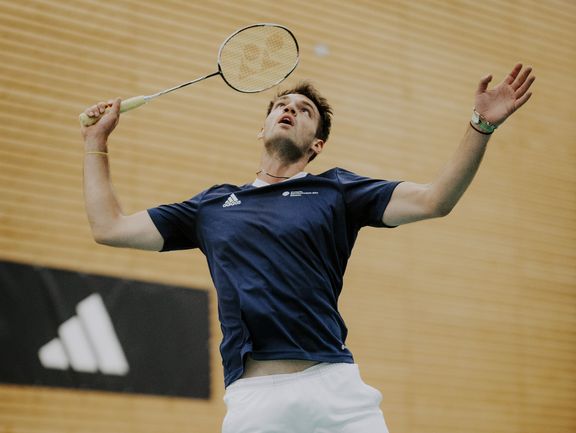 Badmintonspieler in Aktion, im Hintergrund ein adidas-Banner, Spieler trägt adidas-Shirt
