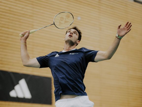 Badmintonspieler in Aktion, im Hintergrund ein adidas-Banner, Spieler trägt adidas-Shirt
