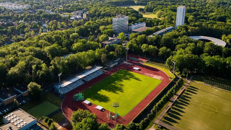 Eine Luftbildaufnahme eines Sportplatzes mit umlaufender Aschenbahn umringt von vielen Bäumen.
