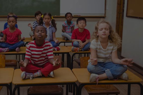 Schüler*innen meditieren mit geschlossenen auf den Schultischen
