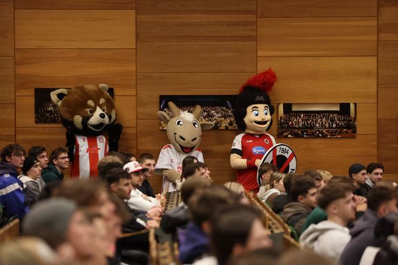 Drei lebensgroße Maskottchen im mit Holz vertäfelten Hörsaal
