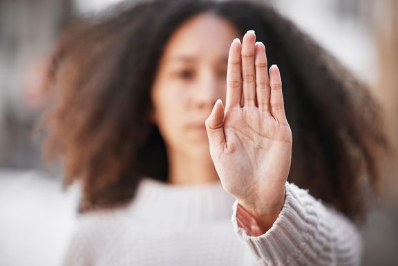 Frau mit dunklen, langen, lockigen Haaren hält linke flache Hand nach vorne gestreckt
