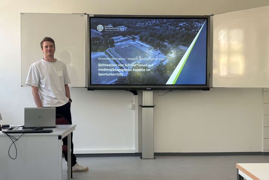 Konstantin Rehlinghaus vor einem Smartboard mit der Titelfolie seiner Präsentation