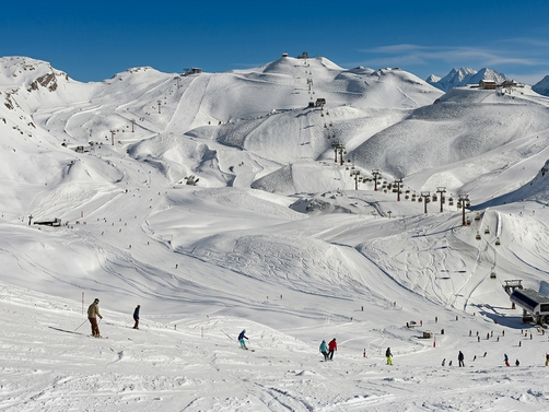 Berglandschaft mit schneebedeckten Pisten, Skiliften und mehreren Skifahrern bei klarem Himmel
