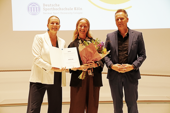 Drei Personen mit einer Urkunde und Blumen
