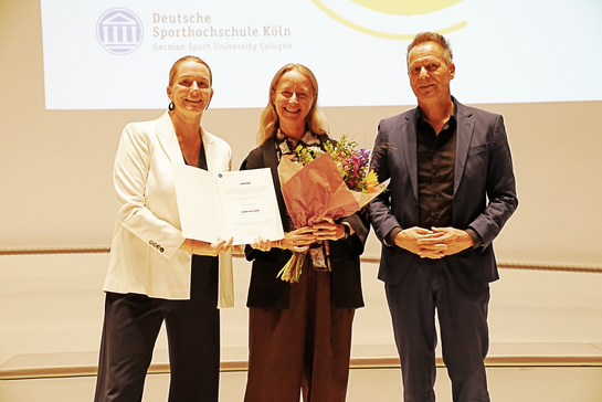 Drei Personen mit einer Urkunde und Blumen
