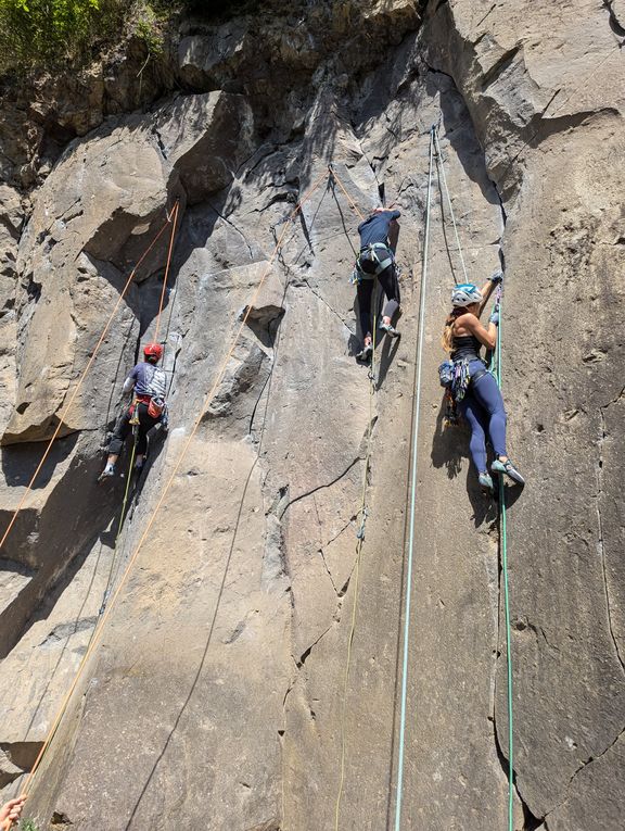 Drei Kletterer mit Helmen und Kletterausrüstung an einer steilen Felswand beim Rissklettern
