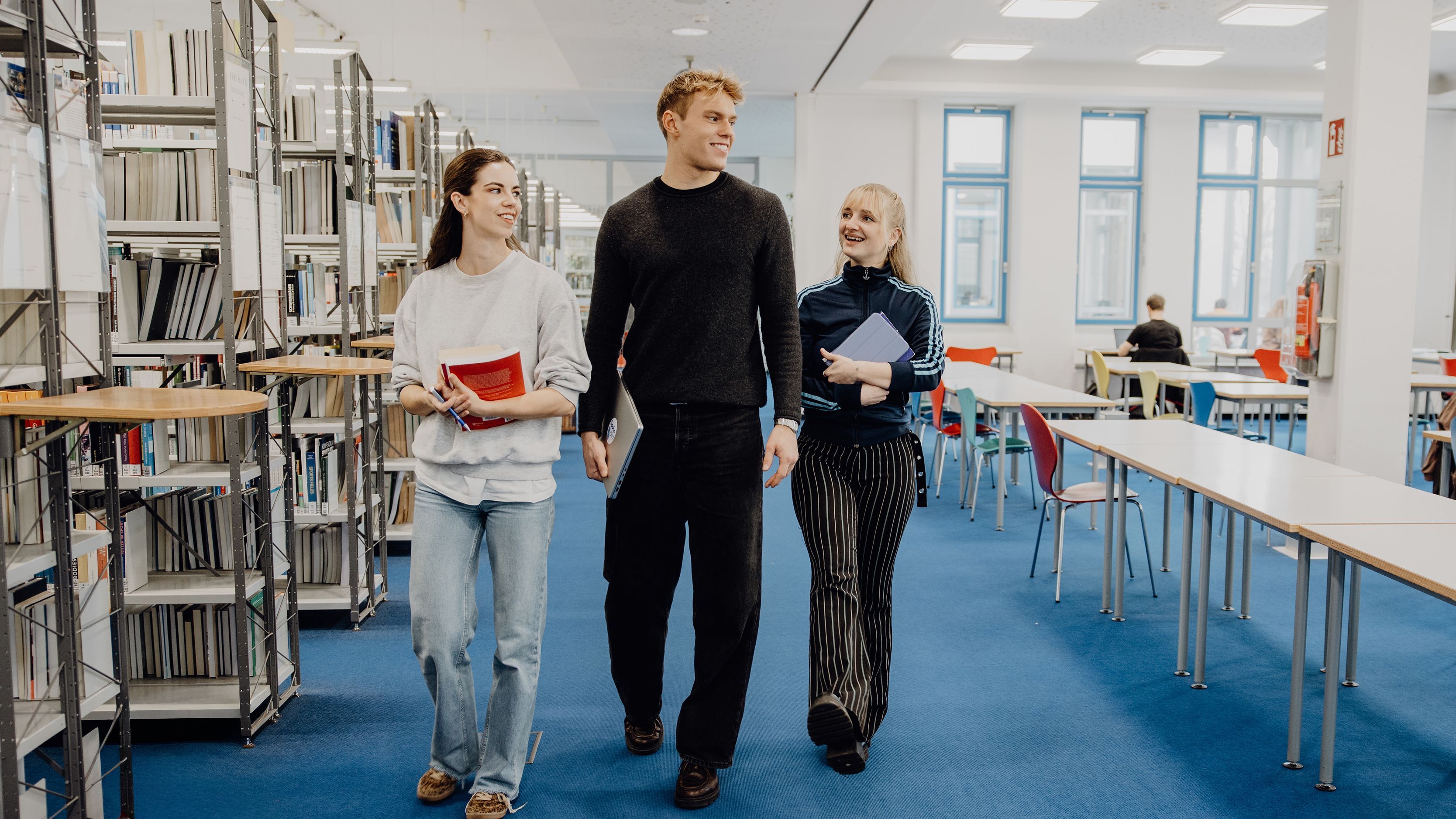 Drei Studierende laufen durch die Bibliothek der Deutschen Sporthochschule
