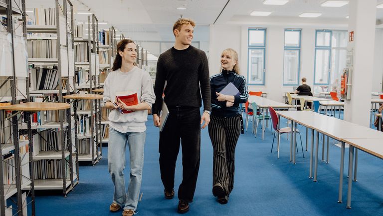 Drei Studierende laufen durch die Bibliothek der Deutschen Sporthochschule

