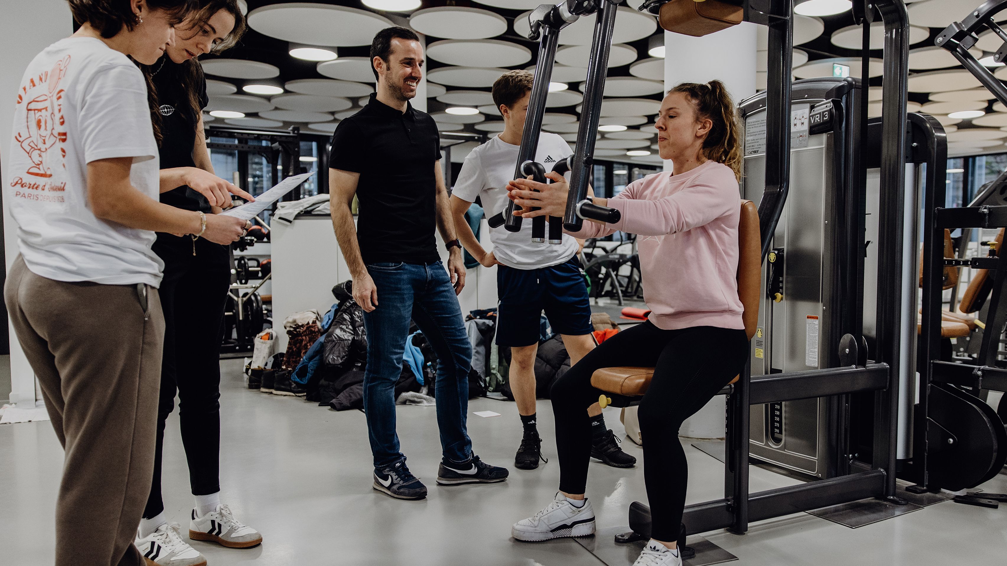 Studierende beobachten Studentin beim Krafttraining 
