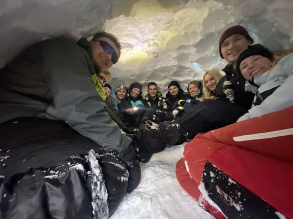 Gruppe von Personen sitzt eng zusammen in einem Iglu aus Schnee und Eis

