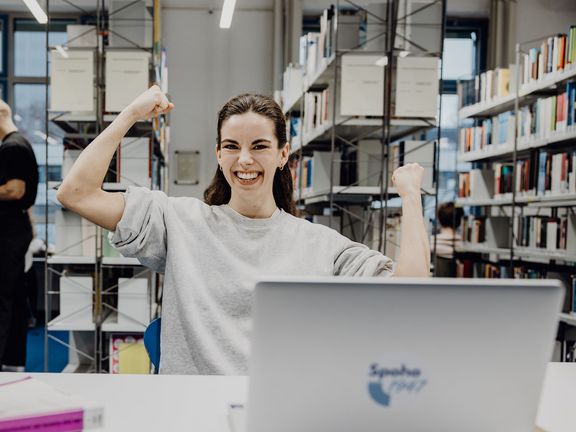 Studentin freut sich mit geballten Fäusten in der Bibliothek

