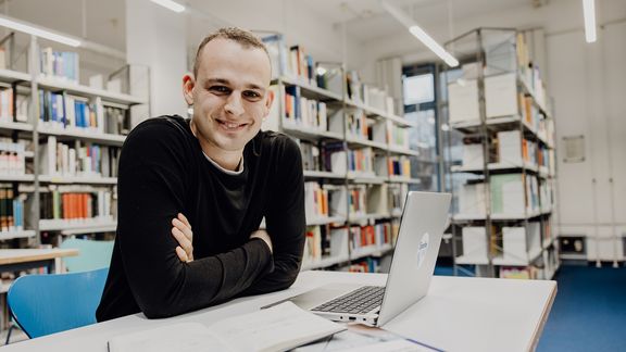 Student sitzt mit Laptop in der Bibliothek der Deutschen Sporthochschule
