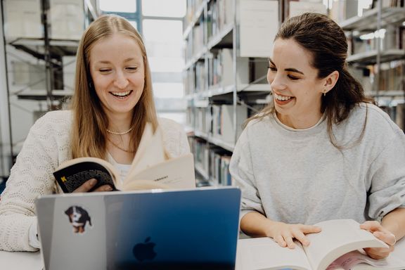 Zwei Studentinnen blättern durch ein Buch in der Bibliothek der Deutschen Sporthochschule
