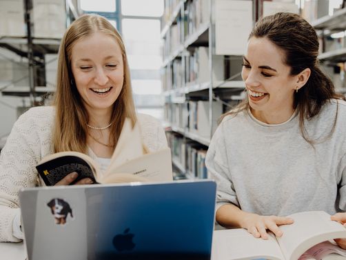 Zwei Studentinnen blättern durch ein Buch in der Bibliothek der Deutschen Sporthochschule

