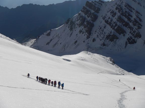 Gruppe von Wanderern mit Rucksäcken auf einem verschneiten Bergweg vor steilen Felswänden
