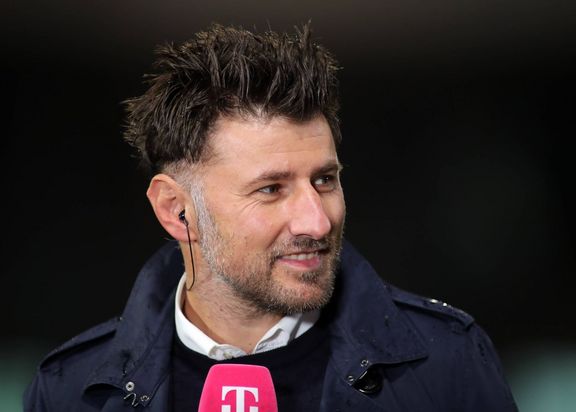 Porträtfoto von Stefan Reisinger. Das Foto zeigt ihn während eines Interviews. Er trägt eine blaue Jacke und hält ein pinkes Mikrofon in der Hand.
