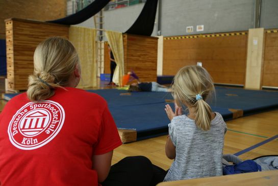 Betreuerin und Kind von hinten in einer Turnhalle
