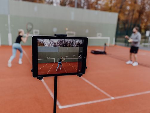 Foto von Tablet das eine Frau die auf einem Tennisplatz gegen eine Wand spielt filmt 
