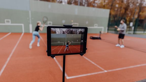 Foto von Tablet das eine Frau die auf einem Tennisplatz gegen eine Wand spielt filmt 
