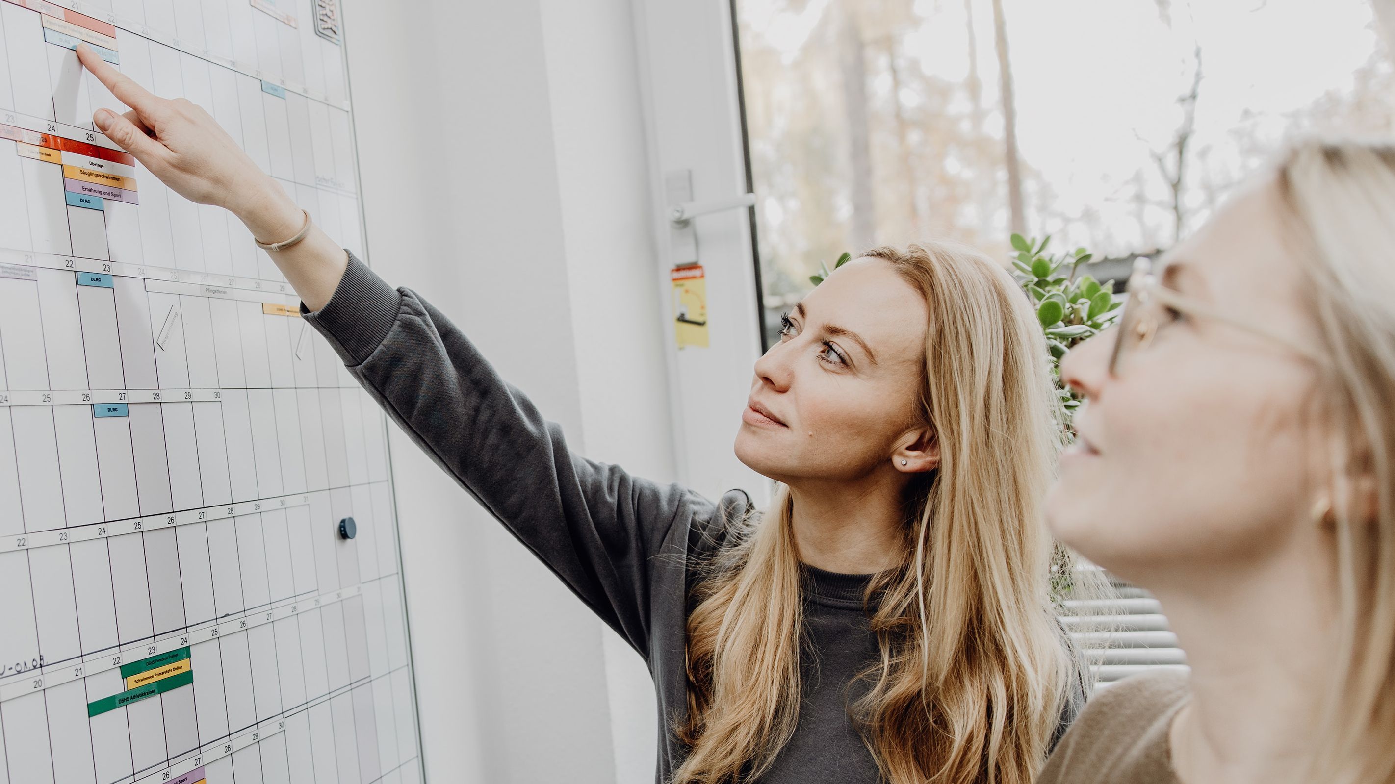 Foto von zwei Frauen die auf Terminkalender an Whiteboard zeigen
