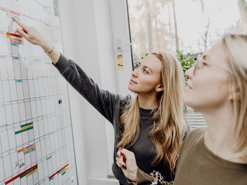 Foto von zwei Frauen die auf Terminkalender an Whiteboard zeigen

