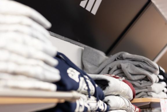 Hoodies und Pullover in den Regalen um SpohoShop, oberhalb der gefalteten Kleidung das Siegel der Spoho und das adidas-Logo
