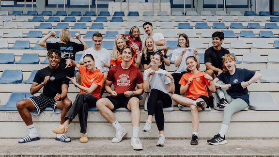 Studierende sitzen auf der Tribüne im Leichtathletikzentrum
