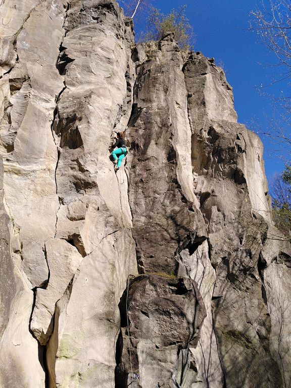 Kletterin in grüner Hose klettert an steiler Felswand im Vorstieg
