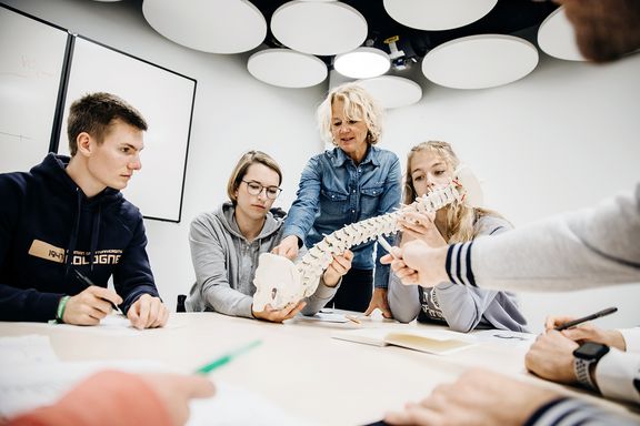  Studierende betrachten in Gruppenarbeit Modell einer Wirbelsäule und eines Beckens
