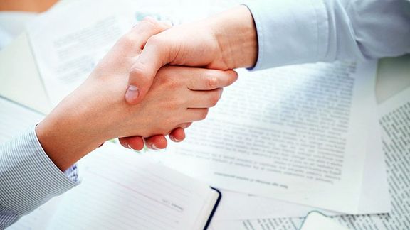 Händeschütteln über einem Tisch mit Texten und Notizen
